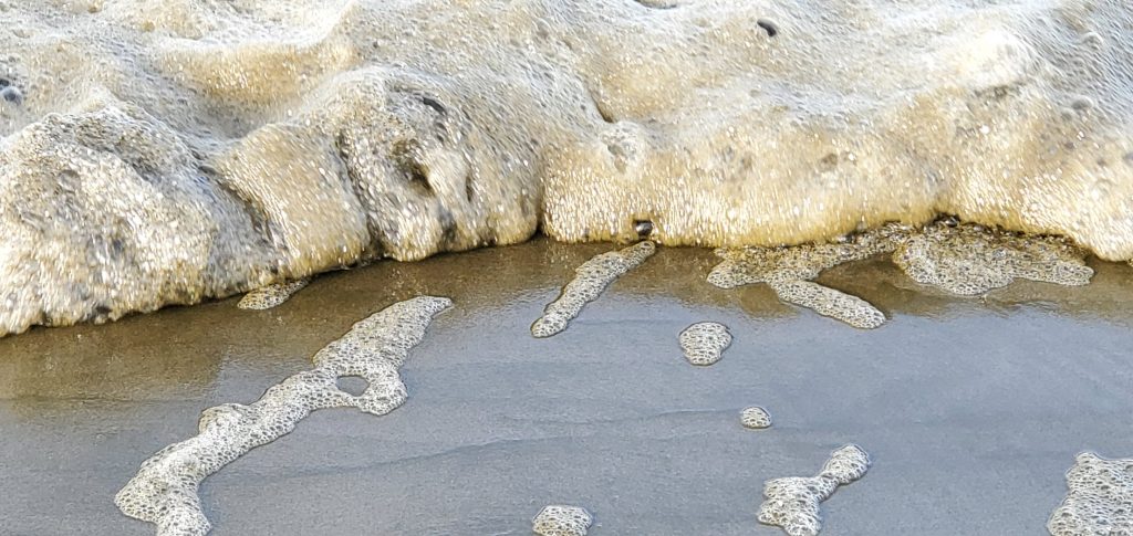 Brown-colored sea foam as a breaker runs out of energy on the beach.